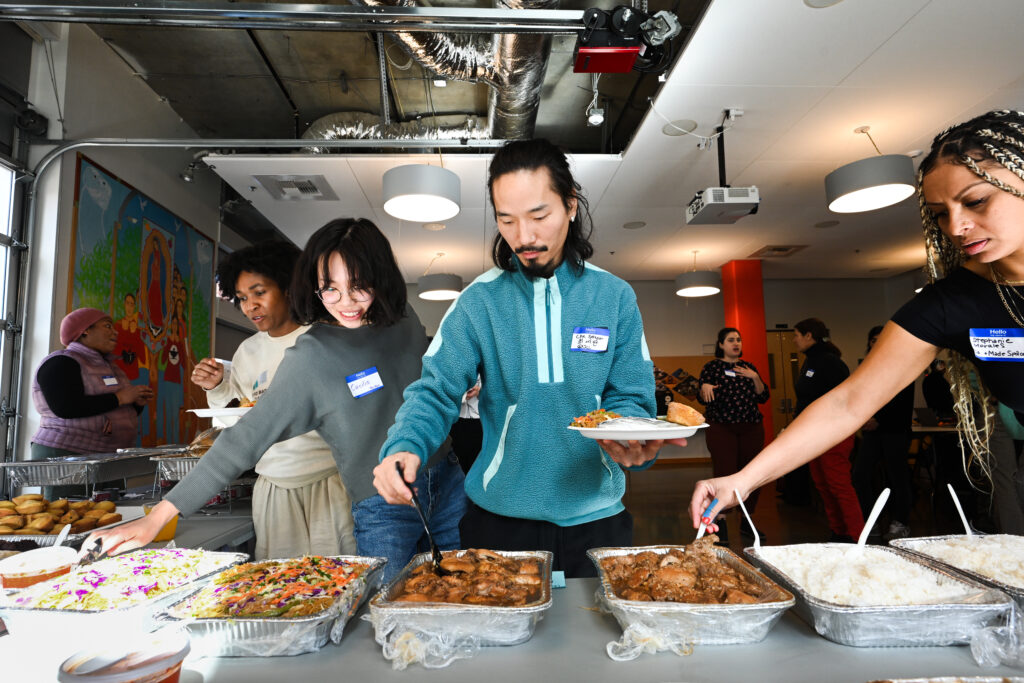 Community Wealth Building workshop participants serve themselves from aluminum plasters filled with Filipino cuisine.